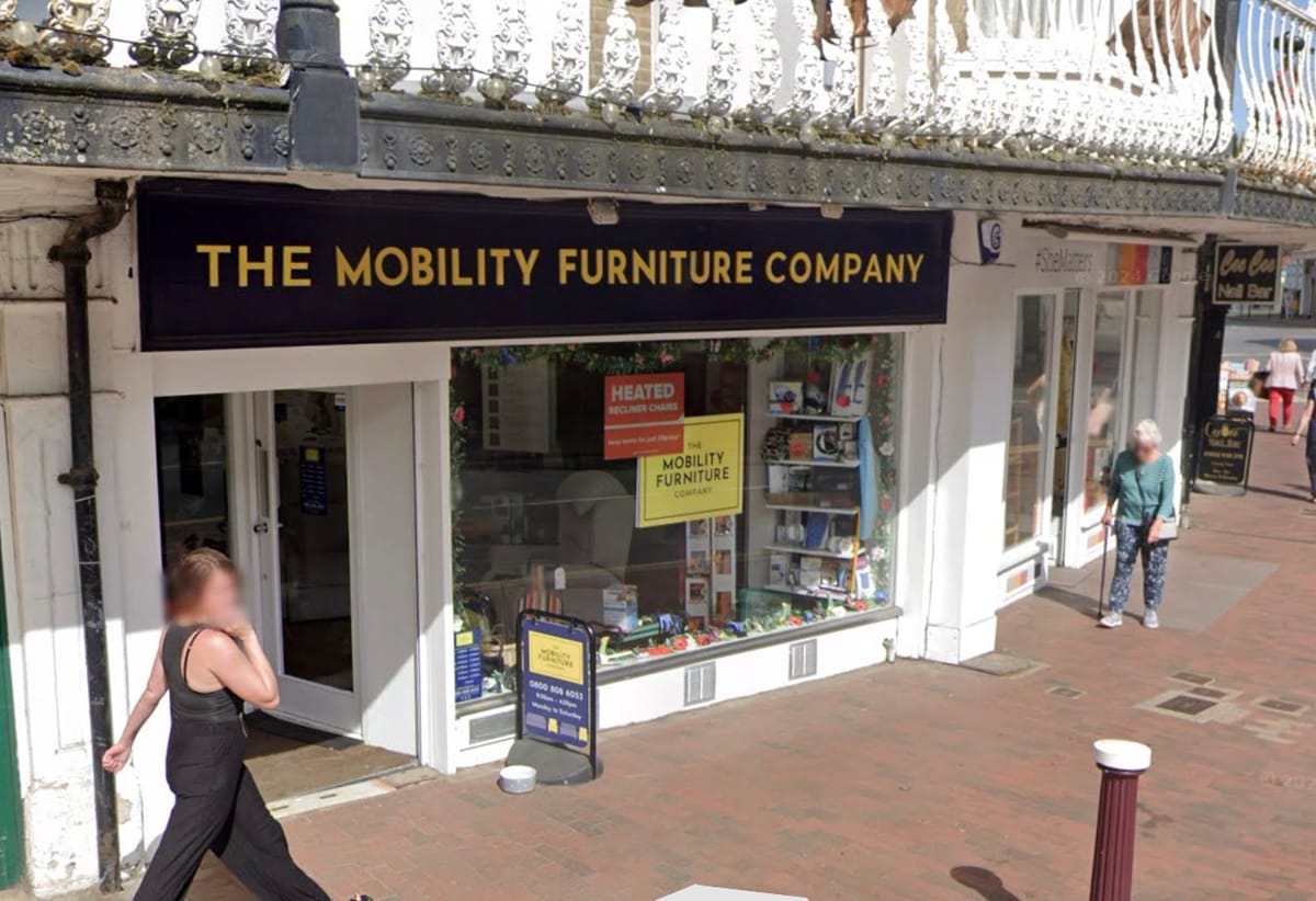 A woman dressed in black in front of a shop, the wording over the shop says Mobility Furniture Company